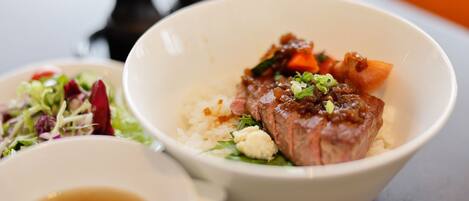 A bowl of food with a piece of meat, vegetables, and rice.