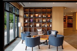 A modern lobby with a seating area featuring blue chairs and a wooden coffee table, surrounded by a bookshelf with various decorative items.