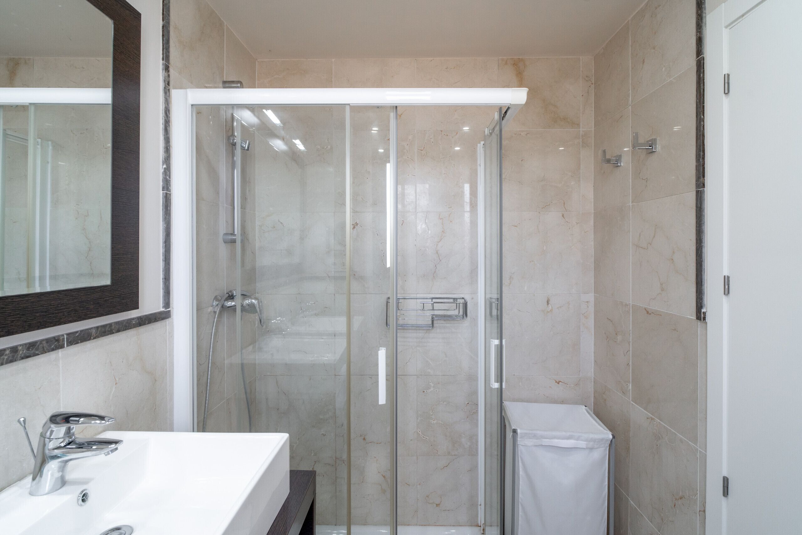 A modern bathroom with a glass-enclosed shower, a white sink, and a mirror above the sink.