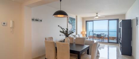 Ein Essbereich mit einem schwarzen Tisch und Stühlen, einer hängenden Pendelleuchte und Blick auf den Balkon.