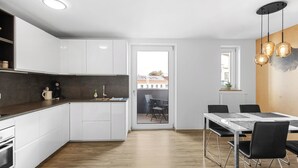 A modern kitchen with white cabinets, a wooden countertop, and a dining area with a table and chairs. - In the middle of Kempten with a mountain feel (Kempten (Allgäu))