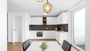 A modern kitchen with white cabinets, a dark countertop, and a built-in oven. There is a dining table with chairs and a potted plant in the center. - In the middle of Kempten with a mountain feel (Kempten (Allgäu))