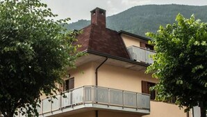A two-story building with a balcony on the upper floor, a stone facade, and a mountain in the background. - Appartamento - Edolo (Edolo)
