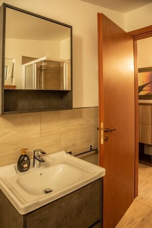 A bathroom with a sink, mirror, and wooden door. - Appartmento 2B - A 20 minuti da Ponte di Legno (Edolo)