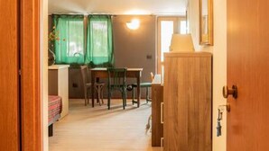 Een smalle gang met houten vloer die uitkomt op een eetgedeelte met een tafel en stoelen.