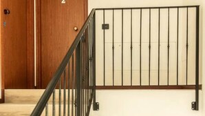 Una escalera con barandilla de metal negro, puertas de madera y pared de color claro.