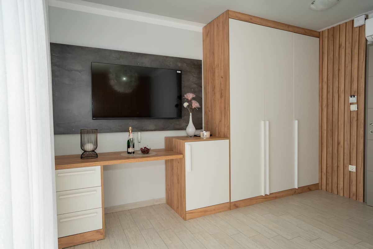 A modern room with a flat-screen TV mounted on a wall, a wooden desk with drawers, a white cabinet, and a wooden panel wall.