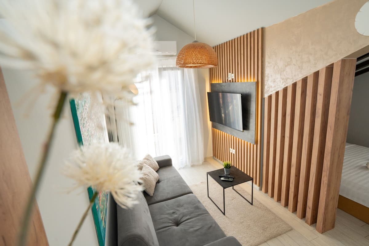 A modern living room with a grey sofa, a small black coffee table, a TV mounted on a wooden panel wall, and a staircase leading to a bedroom.