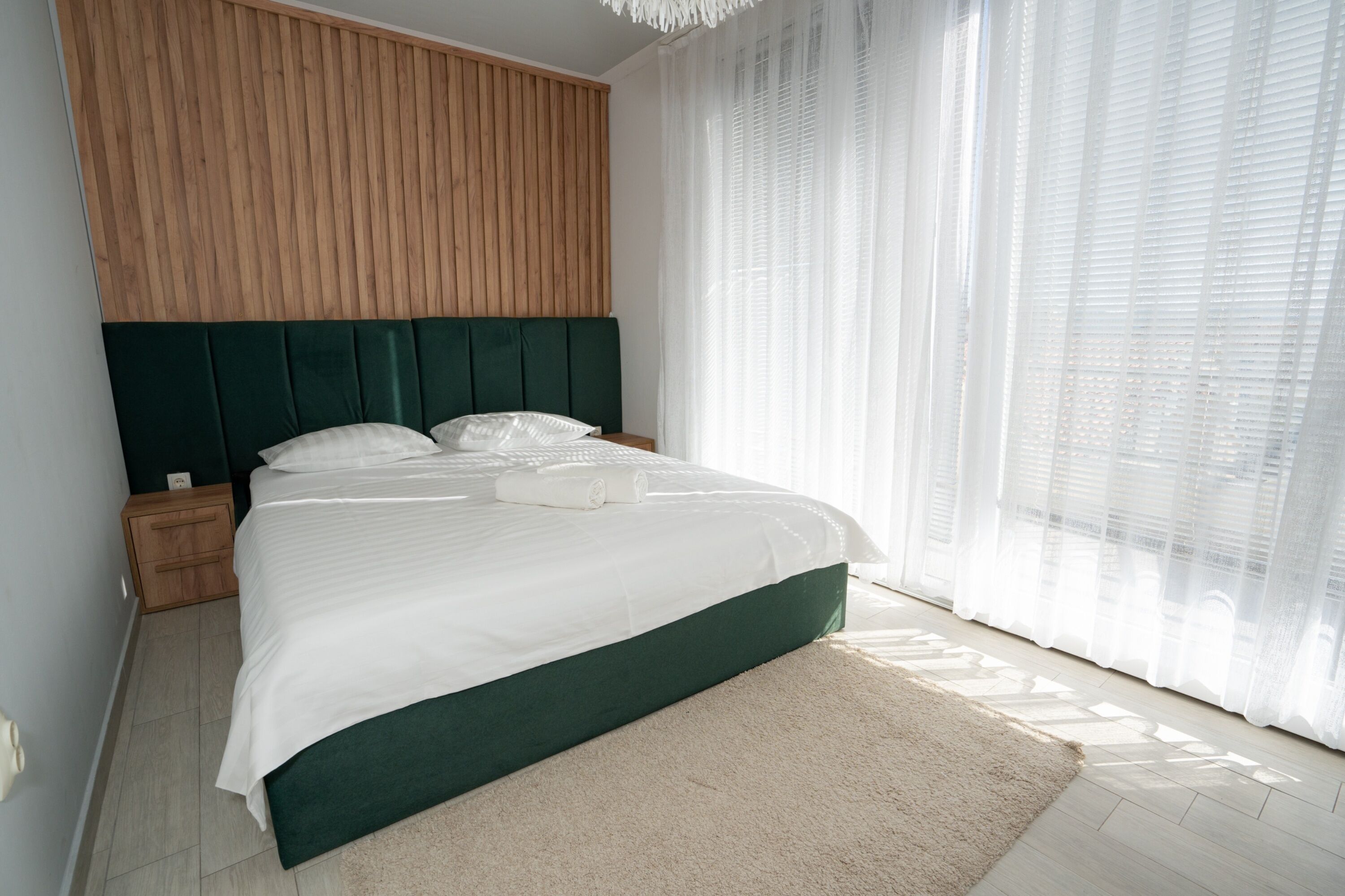 A modern bedroom with a large bed, wooden headboard, and sheer curtains.