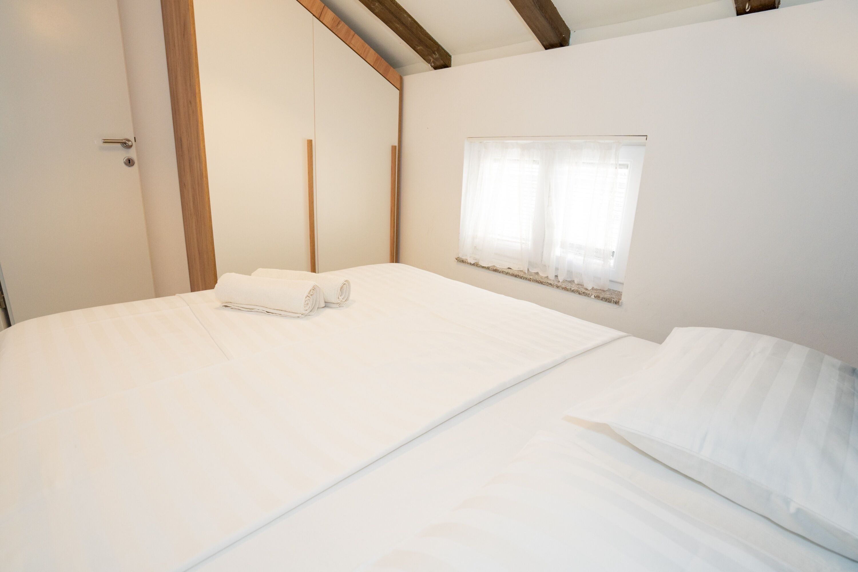 A bedroom with a large bed, a wooden door, and a window with sheer curtains.