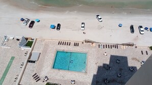 Oversigtsbillede af et strandresort med swimmingpool, strandparasoller og parkerede biler.