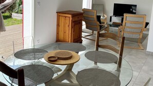 A modern living room with a glass dining table surrounded by chairs, a wooden cabinet, a television, and a painting on the wall.