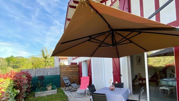 A wooden deck with a table and chairs, a large umbrella, and a view of a house with red and white trim.