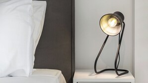 A neatly made bed with white linens and pillows, a modern bedside table with a lamp, and a plain wall. - Relux Sea View Two Bedroom Apartment by BluPine (Athens)