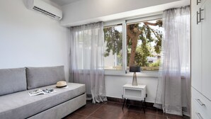 A modern room with a grey sofa, a small table with a lamp, and a window with sheer curtains. - Relux Sea View Two Bedroom Apartment by BluPine (Athens)