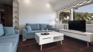 A modern living room with a sofa, a coffee table, a TV, and a bookshelf. - Relux Sea View Two Bedroom Apartment by BluPine (Athens)