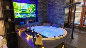 A spa area with a hot tub, a television displaying a nature scene, and various amenities like candles and a bottle of champagne. - Lungomare Suite & Spa (Naples)