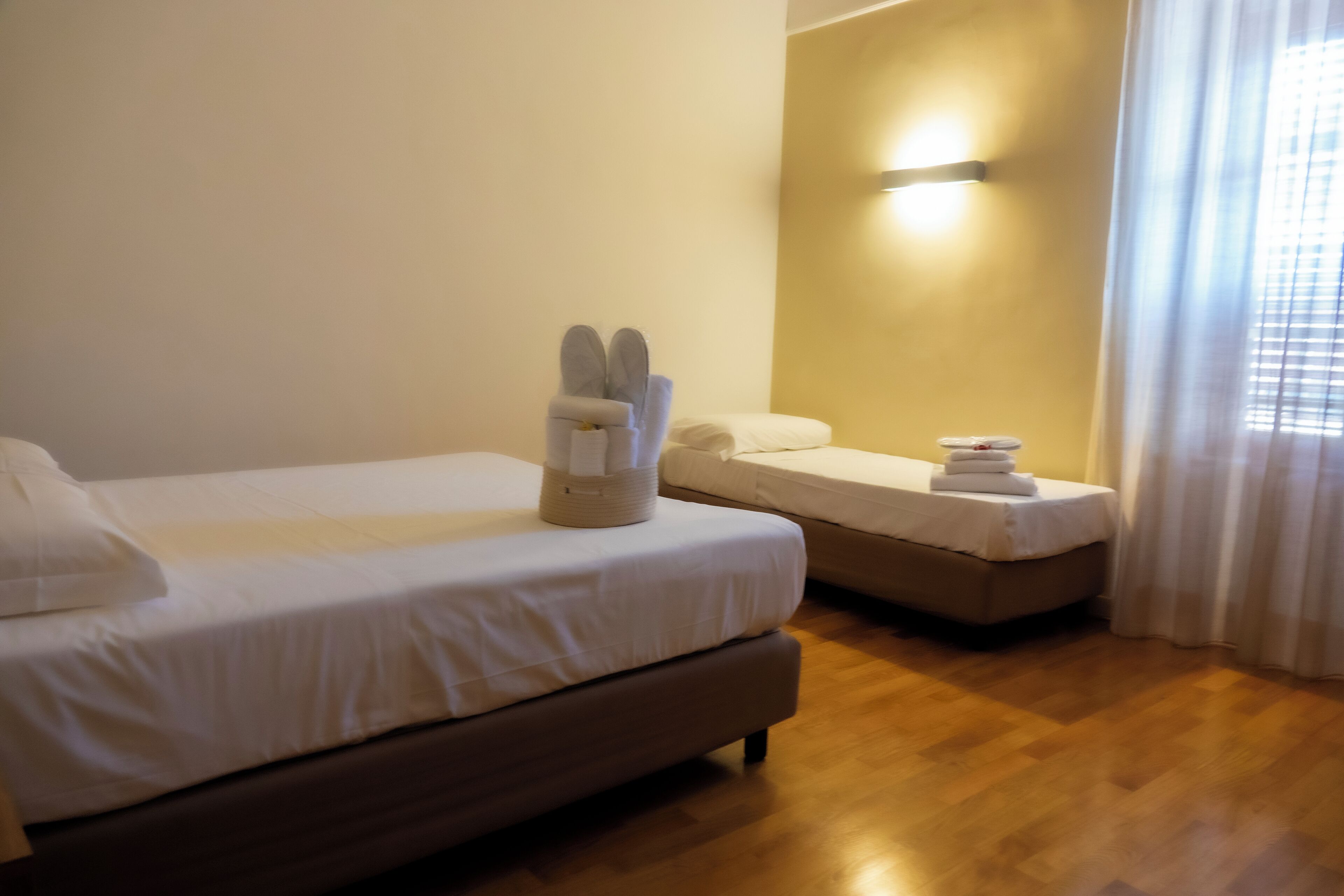 A hotel room with two beds, a wooden floor, and a wall-mounted light fixture.