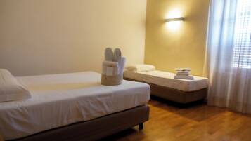 A hotel room with two beds, a wooden floor, and a wall-mounted light fixture.