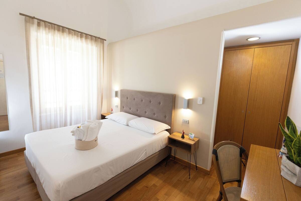 Habitación de hotel ordenada con una cama grande, mesitas de noche, una silla y un armario de madera.
