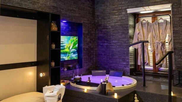 A modern spa room with a bed, a hot tub, and a TV screen. - Lungomare Suite & Spa (Naples)