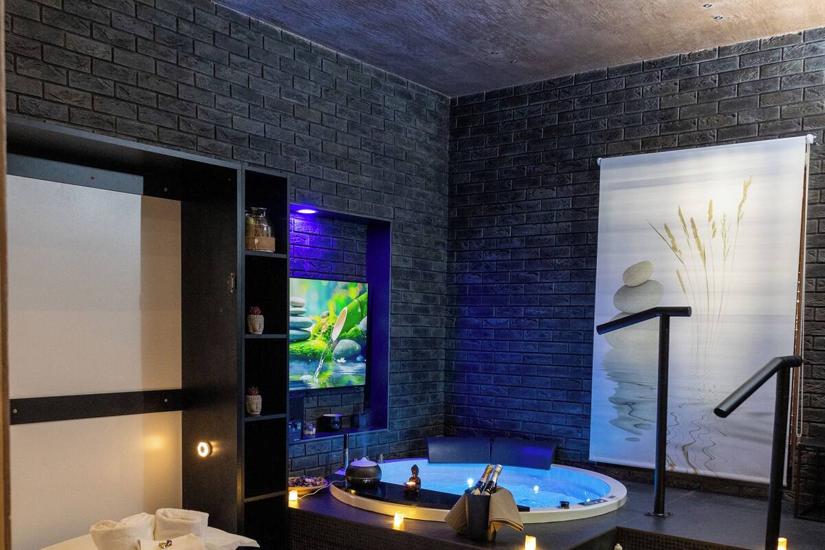 Una habitación de hotel moderna con una cama grande, una pequeña zona de estar, una bañera y un televisor.