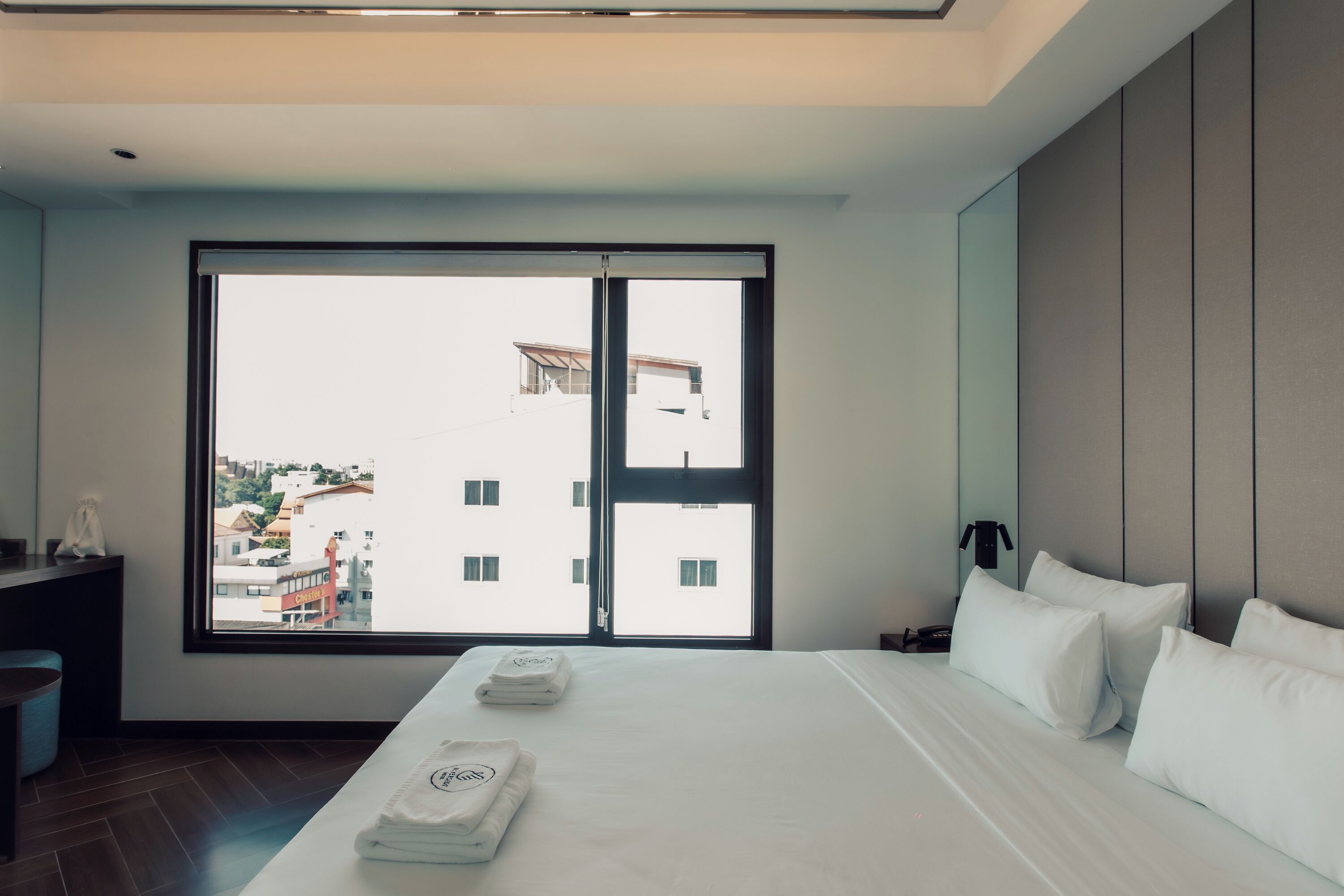 A modern hotel room with a large window, a neatly made bed, and a view of the cityscape.