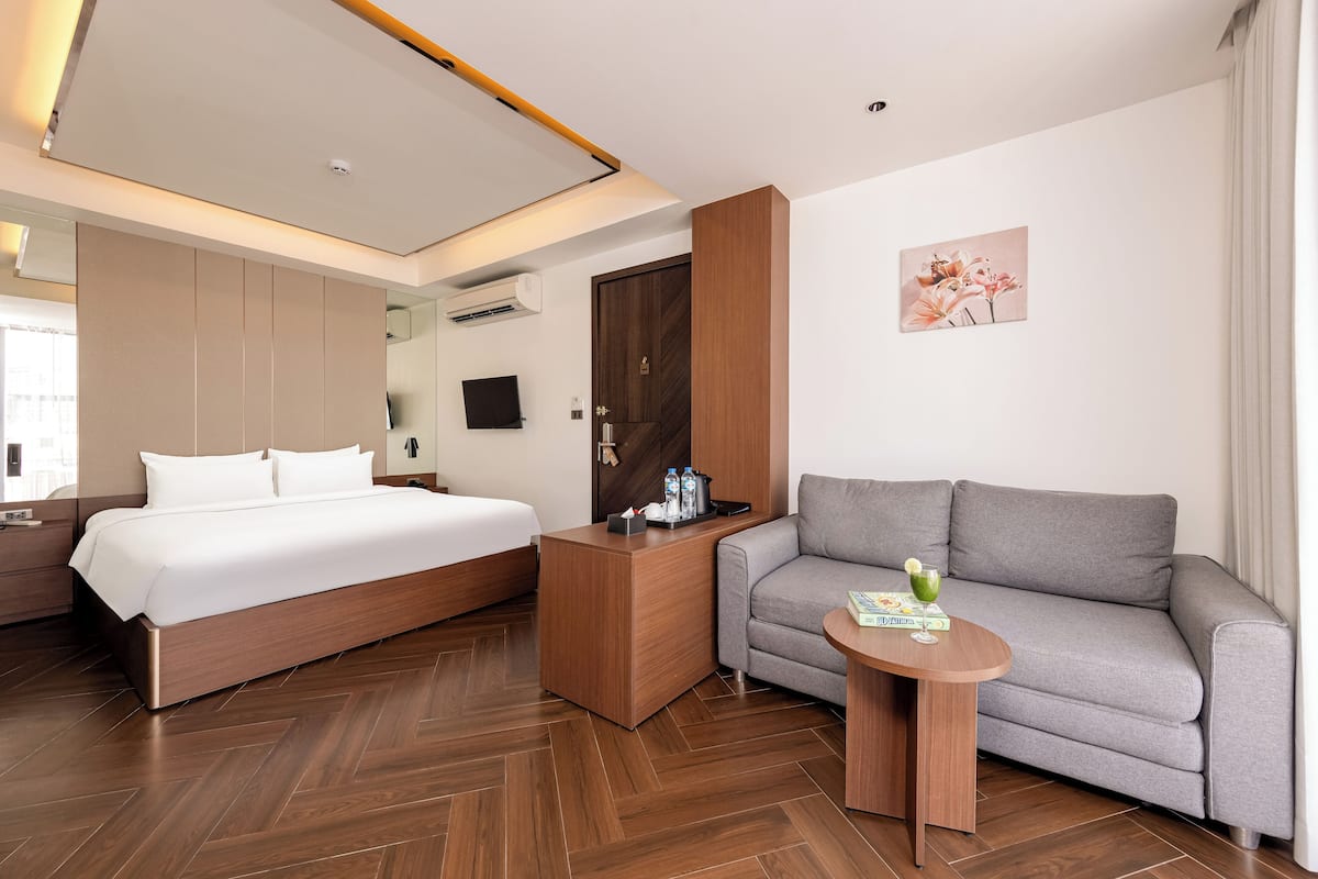 A modern hotel room with a large bed, a sofa, a small table, and a TV.