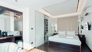 A modern hotel room with a large bed, a bedside table, a chair, a wardrobe with a mirror, and a small desk with a coffee maker and bottles. - Riverside Hotel (Vientiane)