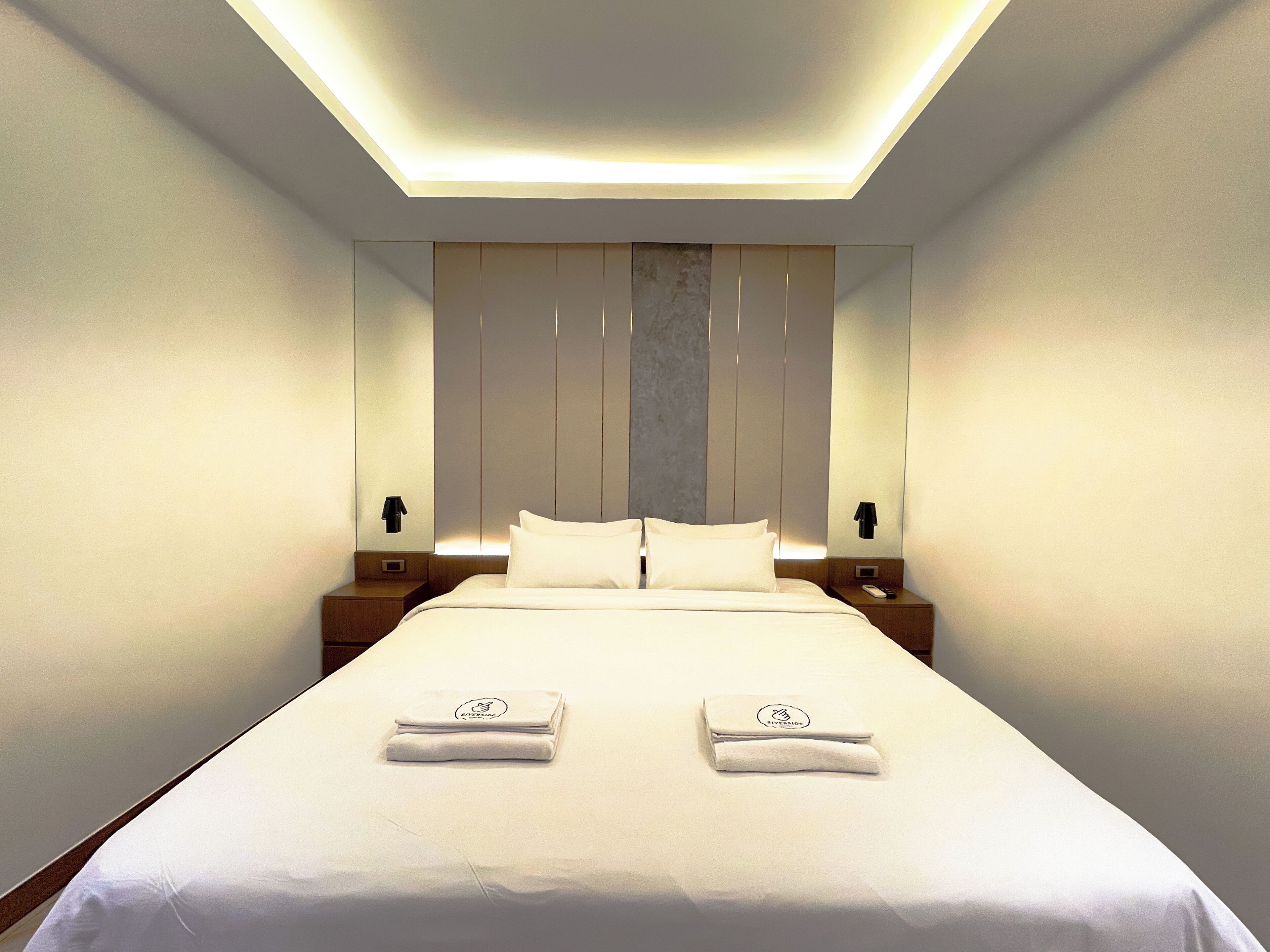 Una habitación de hotel moderna con una cama bien hecha, dos mesitas de noche y un espejo grande sobre la cama.