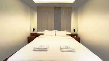 Una habitación de hotel moderna con una cama bien hecha, dos mesitas de noche y un espejo grande sobre la cama.
