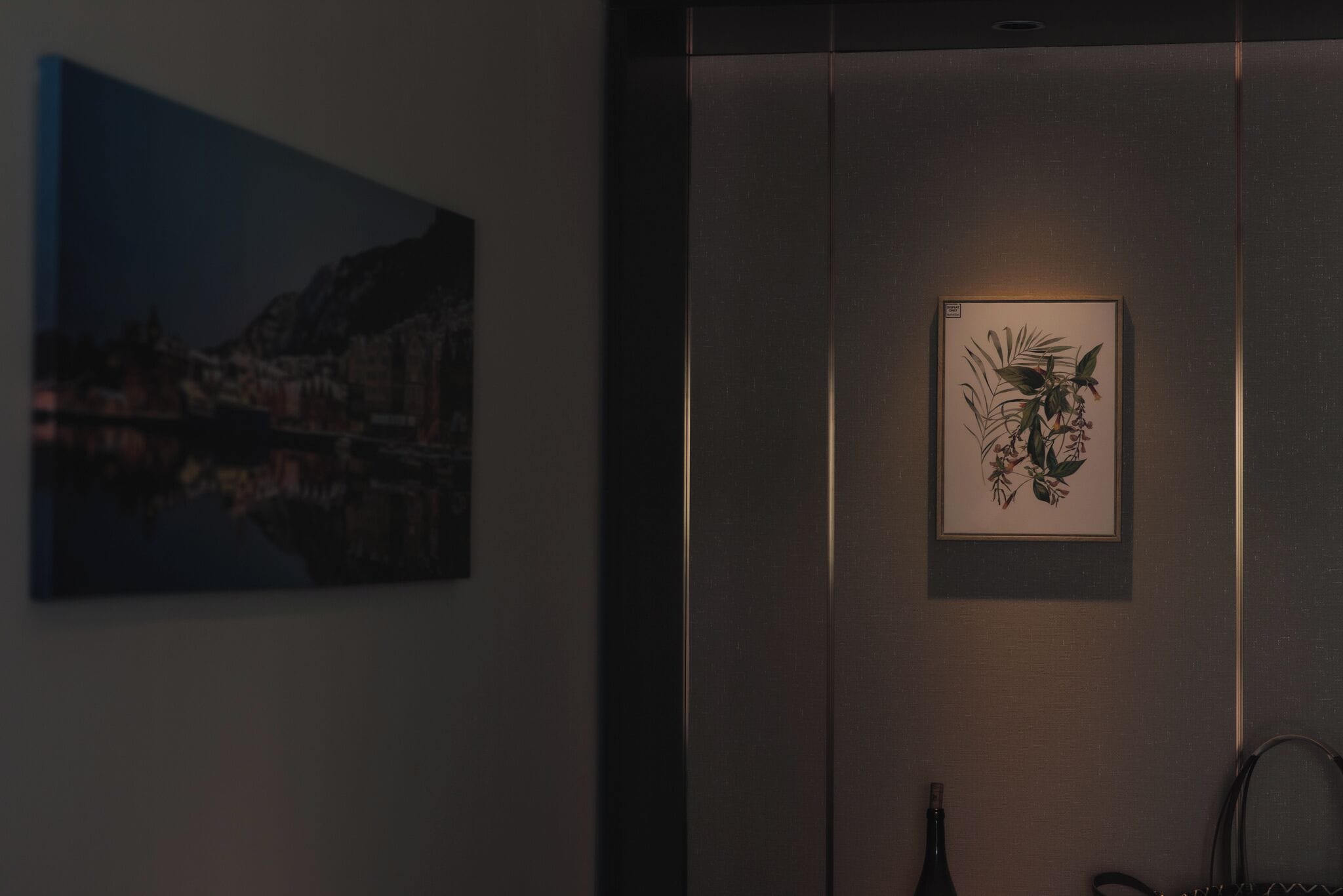 A dimly lit room with a framed artwork on the wall and a vase on the floor.