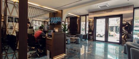 A modern hotel lobby with a reception desk, seating area, and large windows offering city views.