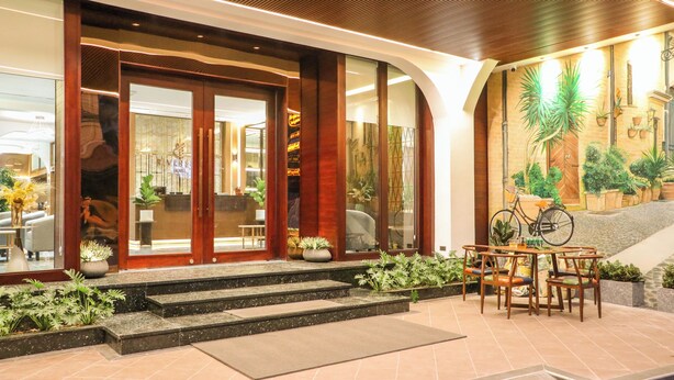 A hotel entrance with a wooden facade, steps leading up to the door, and a seating area with chairs and a table. - Riverside Hotel (Vientiane)