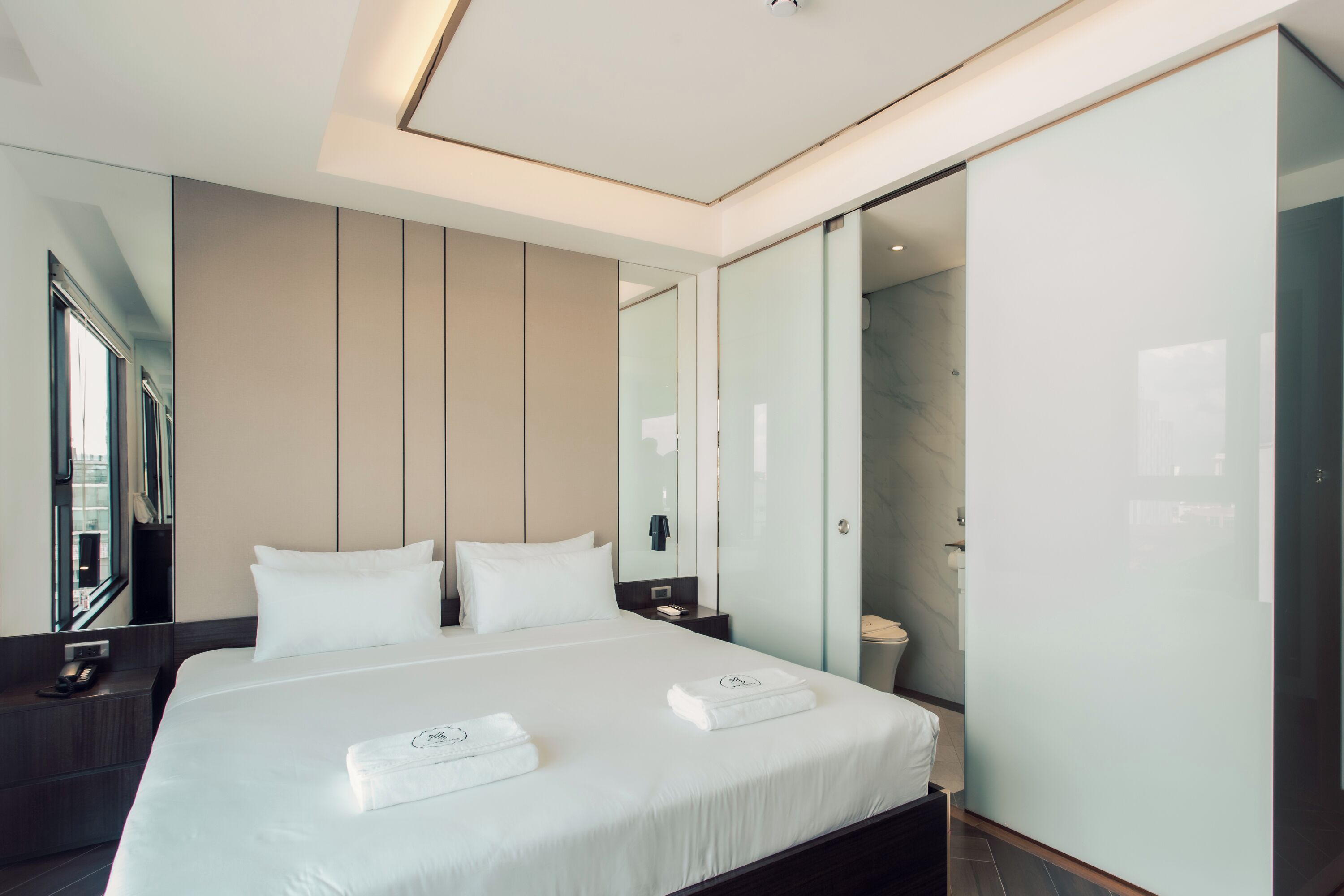 A modern hotel room with a large bed, a bedside table, a mirror, and a glass shower enclosure.