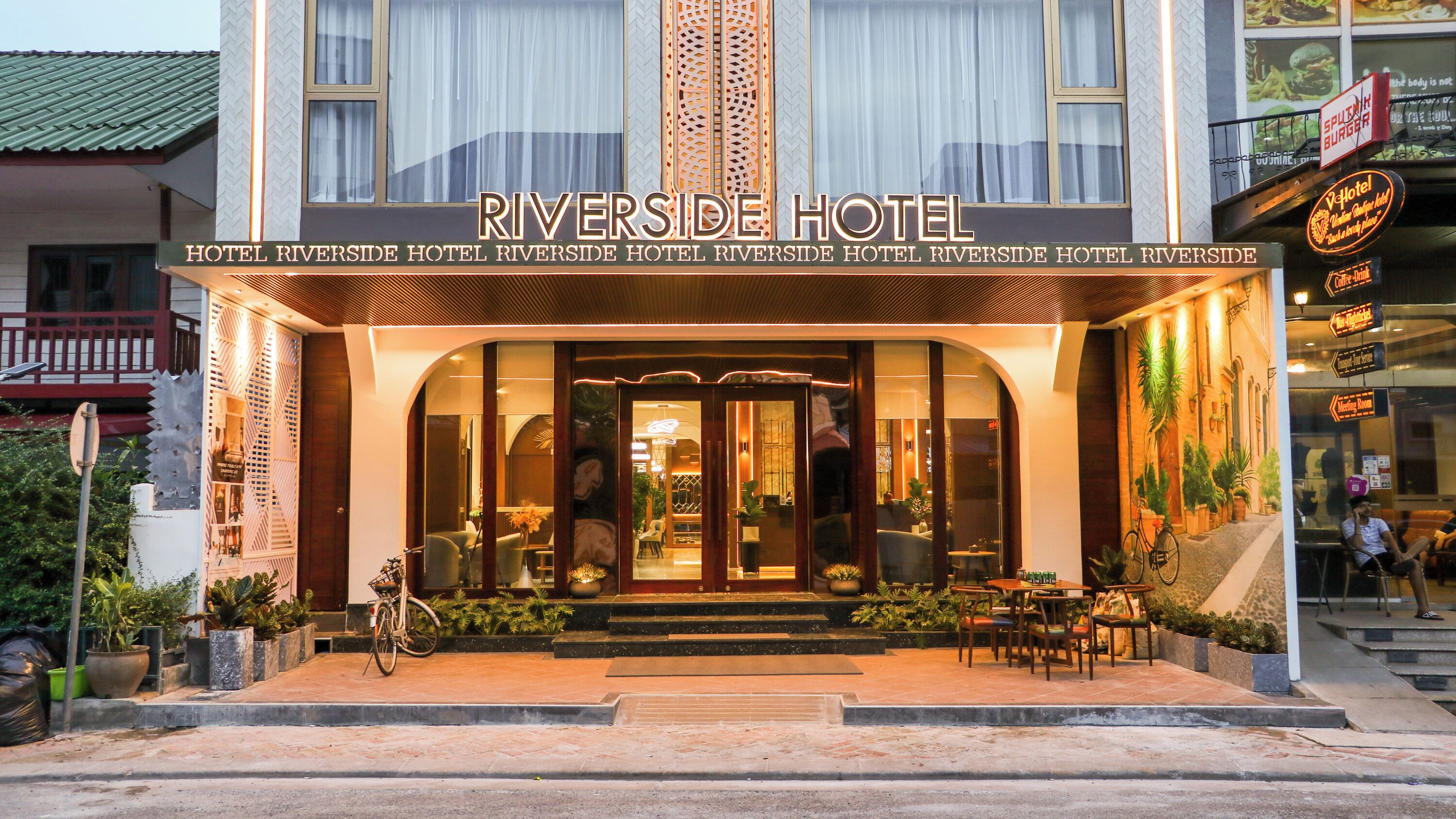 The exterior of Riverside Hotel with a prominent entrance, a bicycle parked in front, and outdoor seating area.