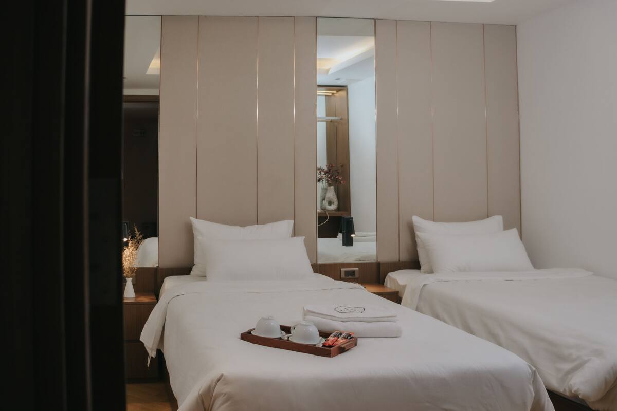 A hotel room with two beds, a mirror, and a tray with a teapot and cups.