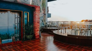 An outdoor dining area with white chairs and tables, a potted plant, and a mural on the wall. - Riverside Hotel (Vientiane)