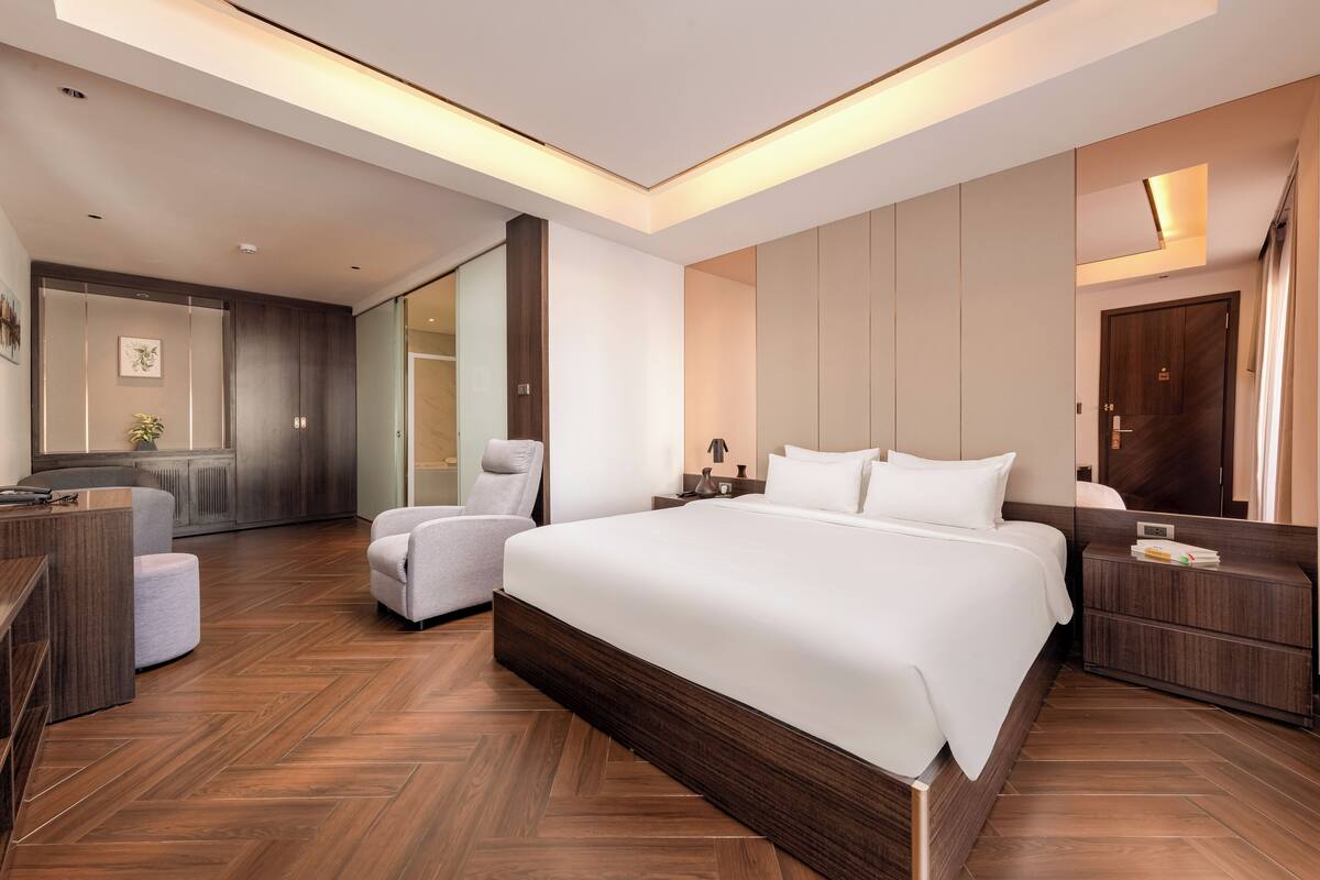 A modern hotel room with a large bed, a desk, a chair, and a wardrobe.