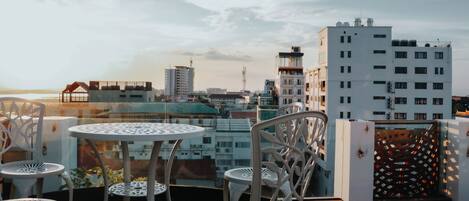 A rooftop terrace with a view of the city skyline, featuring a table and chairs, and a decorative metal fence.
