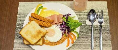 A plate with toast, a fried egg, ham, and vegetables, accompanied by a glass of water and cutlery on a placemat.