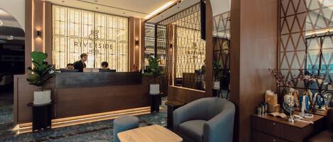 Zona de recepción de un hotel con diseño moderno, que incluye mostrador de recepción, área de estar y plantas decorativas.