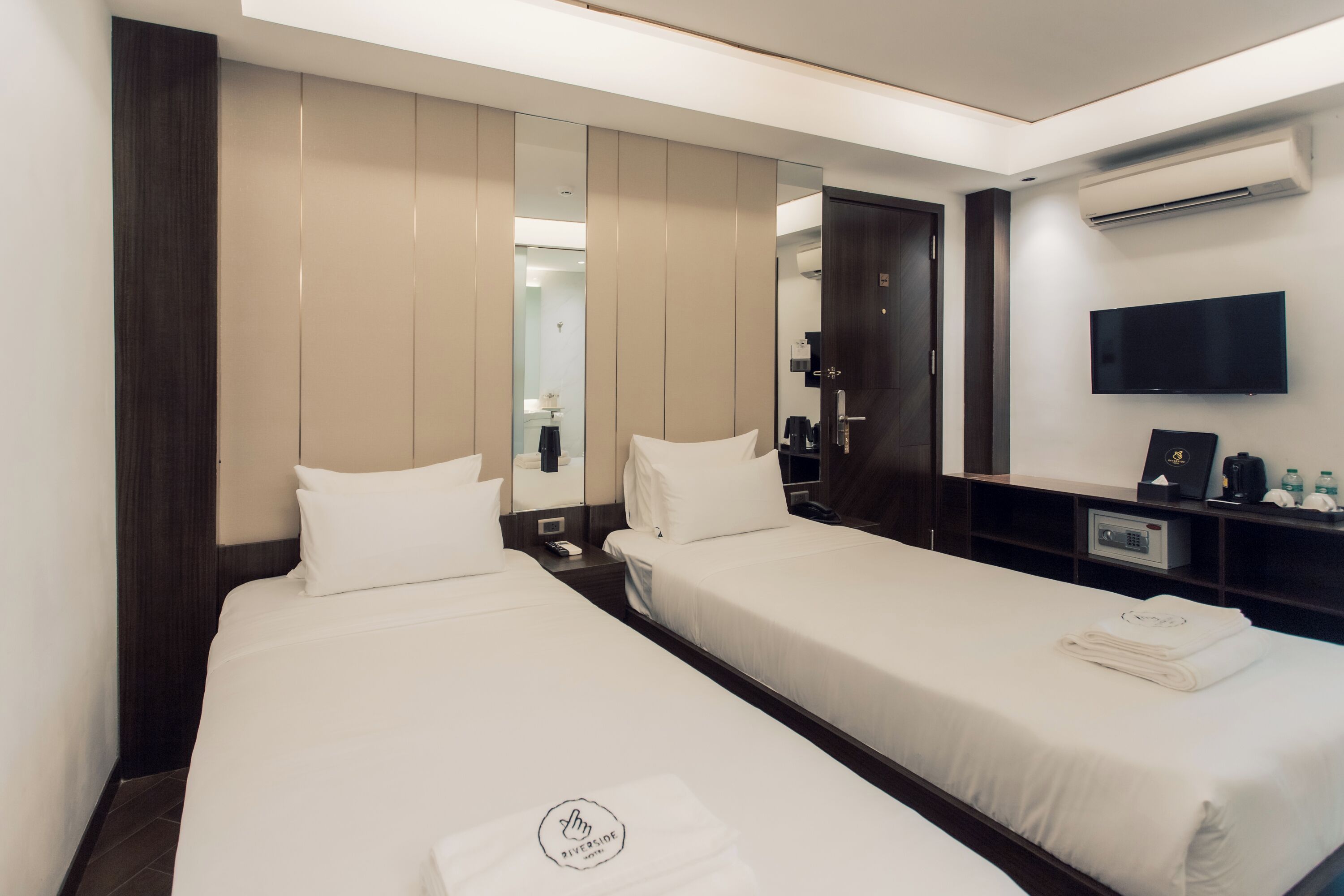 A hotel room with two beds, a TV, a mirror, and a wardrobe.