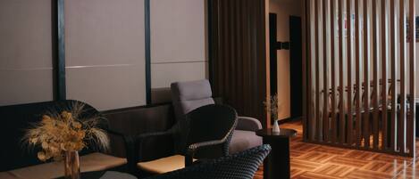 A modern waiting area with a sofa, chairs, a small table with a vase, and a wooden floor.