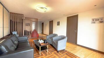 A modern hotel room with a sofa, armchairs, a small table, and a wooden floor.