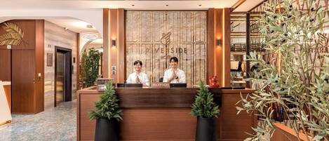 A hotel reception desk with two staff members, a reception area, and a reception sign.