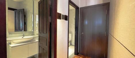Un pasillo con suelo de madera, un espejo, un lavamanos y una puerta que da a un baño.