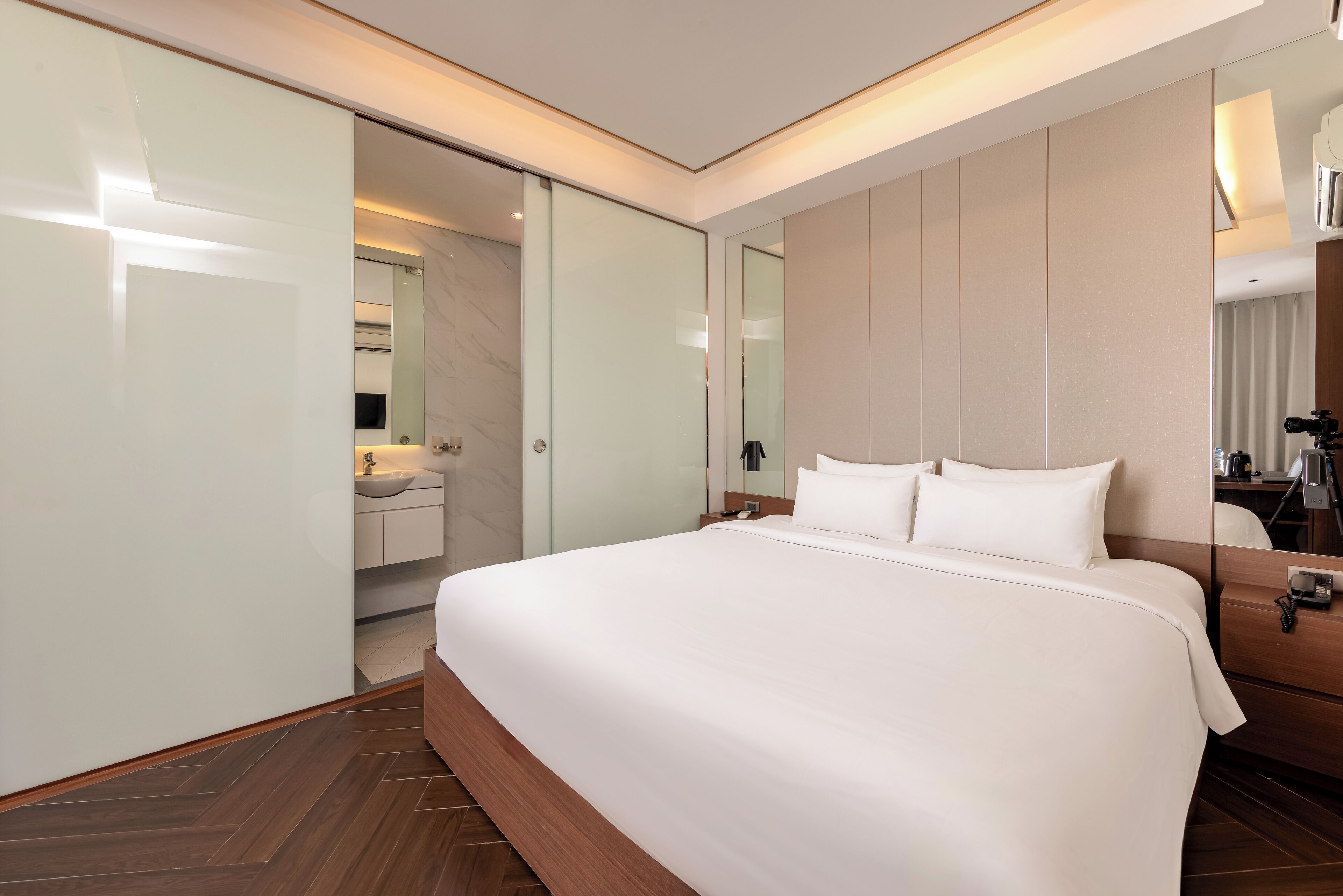 A modern hotel room with a large bed, a walk-in closet, a bathroom with a vanity, and a large mirror.