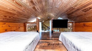 Ein gemütliches Schlafzimmer im Dachgeschoss mit Holzwänden und schrägen Wänden, mit zwei Betten und einem großen Fernseher.