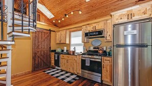 Eine Küche mit Holzausstattung, einem Edelstahlkühlschrank, einem Herd und einer Holztreppe.